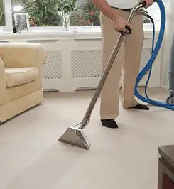 Professional carpet cleaner using a hot-water extraction wand and hose machine in a living room in Nashville, TN.