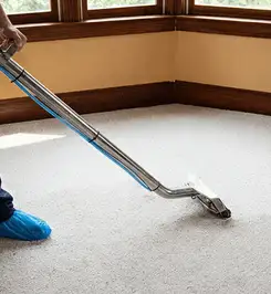 Steam carpet cleaning technician using a hot-water extraction wand on a residential carpet, wearing blue protective shoe covers Nashville, TN.