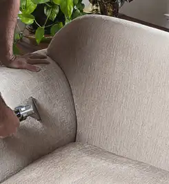 Professional upholstery cleaner deep-cleaning a fabric sofa with a handheld extraction tool and hose Nashville, TN.